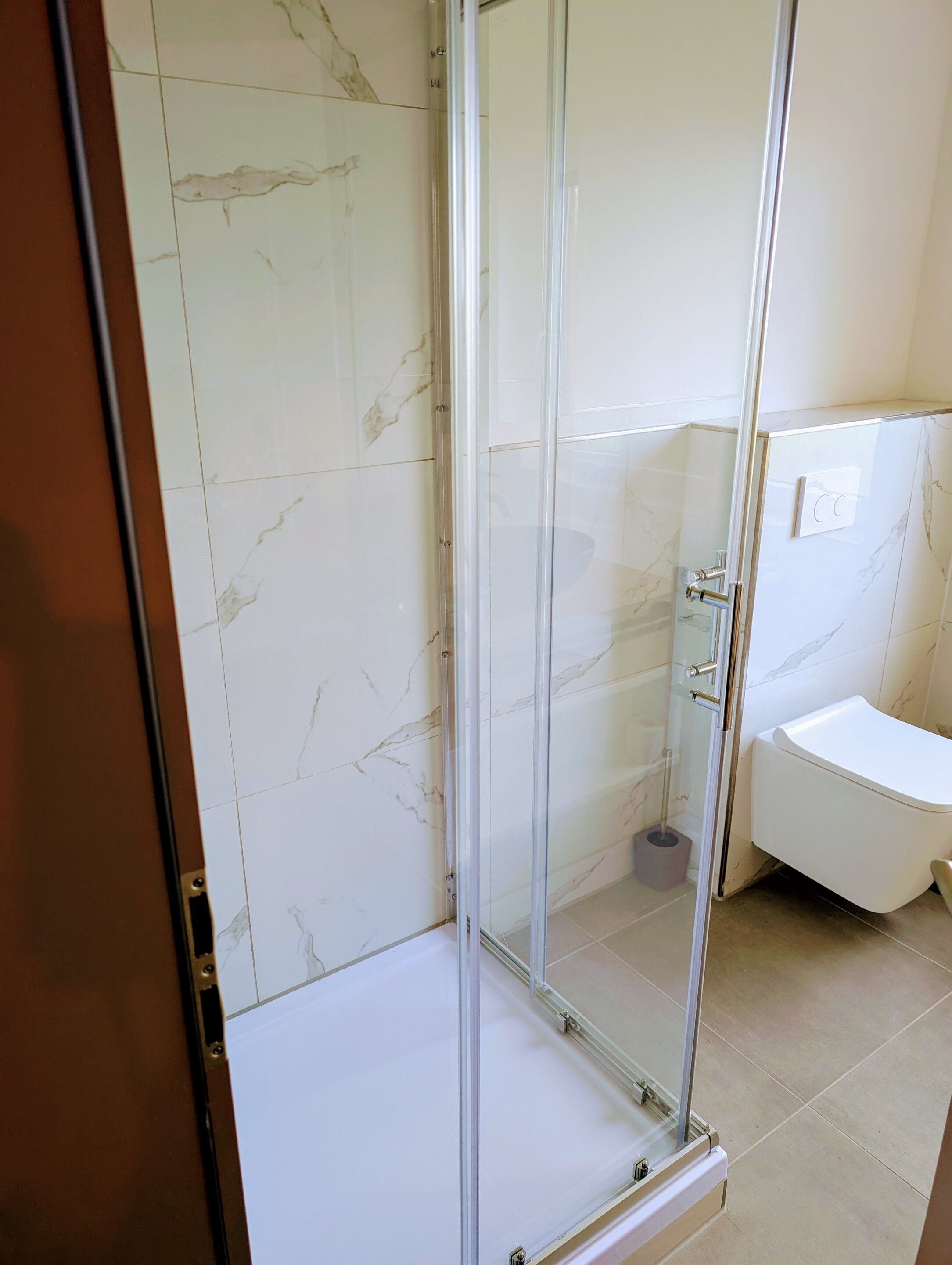 A bathroom with a glass-enclosed shower, a toilet, and marble-tiled walls.