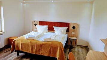 A hotel room with a bed, a wooden headboard, a small stool, and a wooden table.