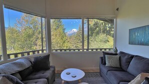 Un salon chaleureux avec un canapé et deux petites tables, de grandes fenêtres offrant une vue sur les montagnes.