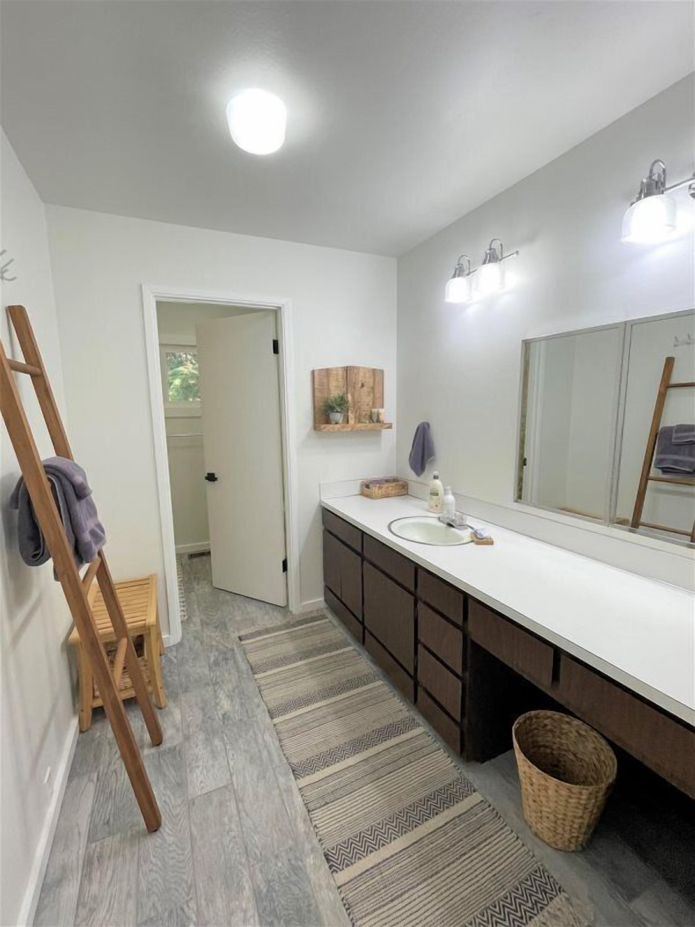A modern bathroom with a white vanity, dark cabinets, a large mirror, and a wooden ladder.