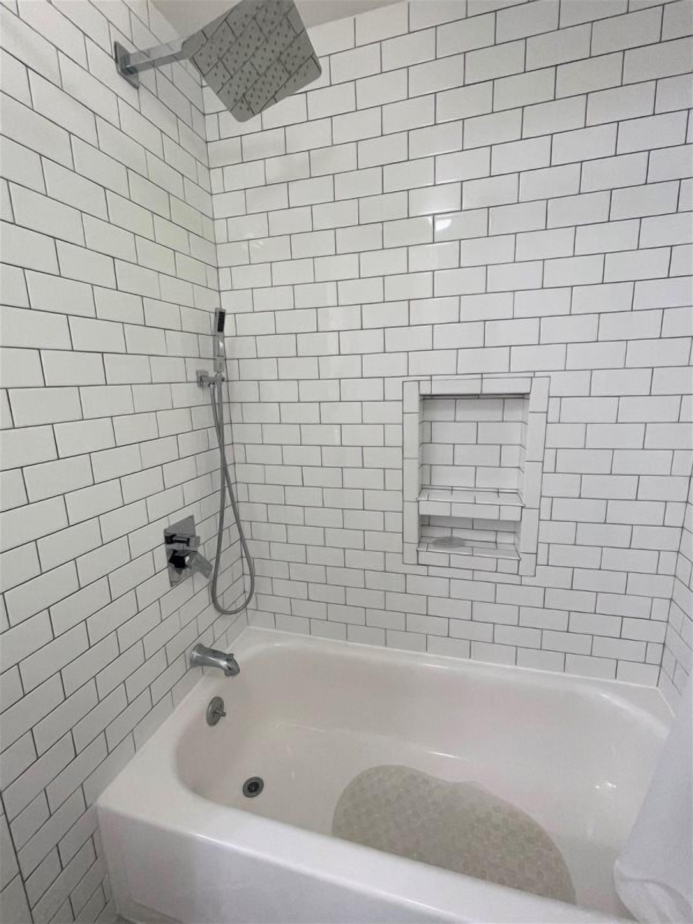 A bathroom with white subway tiles, a bathtub, a showerhead, and a towel rack.