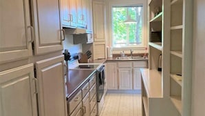 Une cuisine avec des meubles blancs, une cuisinière, un évier et une fenêtre qui laisse entrer la lumière naturelle.