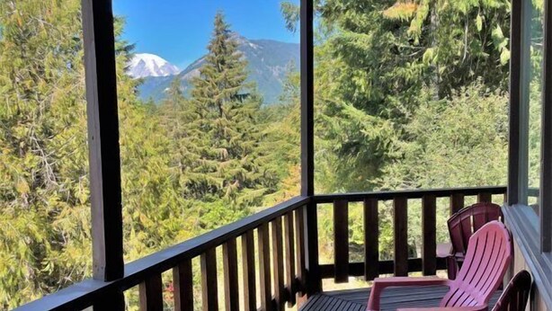 Une terrasse en bois avec deux fauteuils Adirondack donnant sur une vue sur les montagnes.