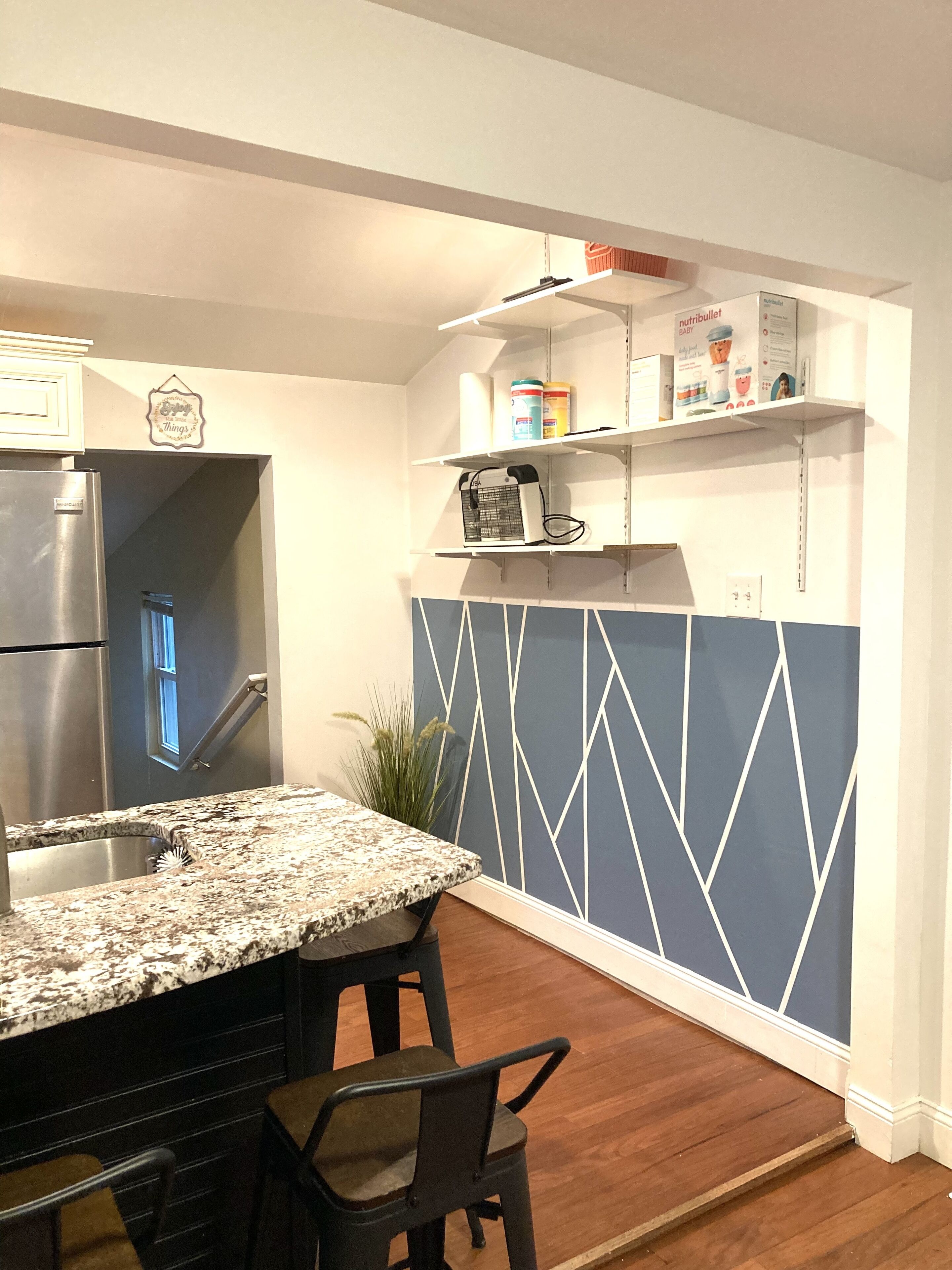 A kitchen with a granite countertop, a stainless steel refrigerator, and a blue accent wall.