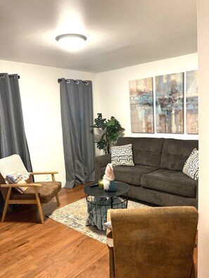 A living room with a grey sofa, a wooden chair, a round coffee table, and a grey rug.