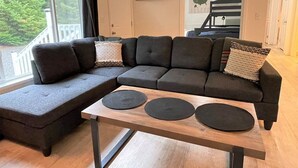 Una sala de estar moderna con un sofá modular, una mesa de centro de madera con tres alfombras redondas y un ventanal con vistas a zonas verdes.