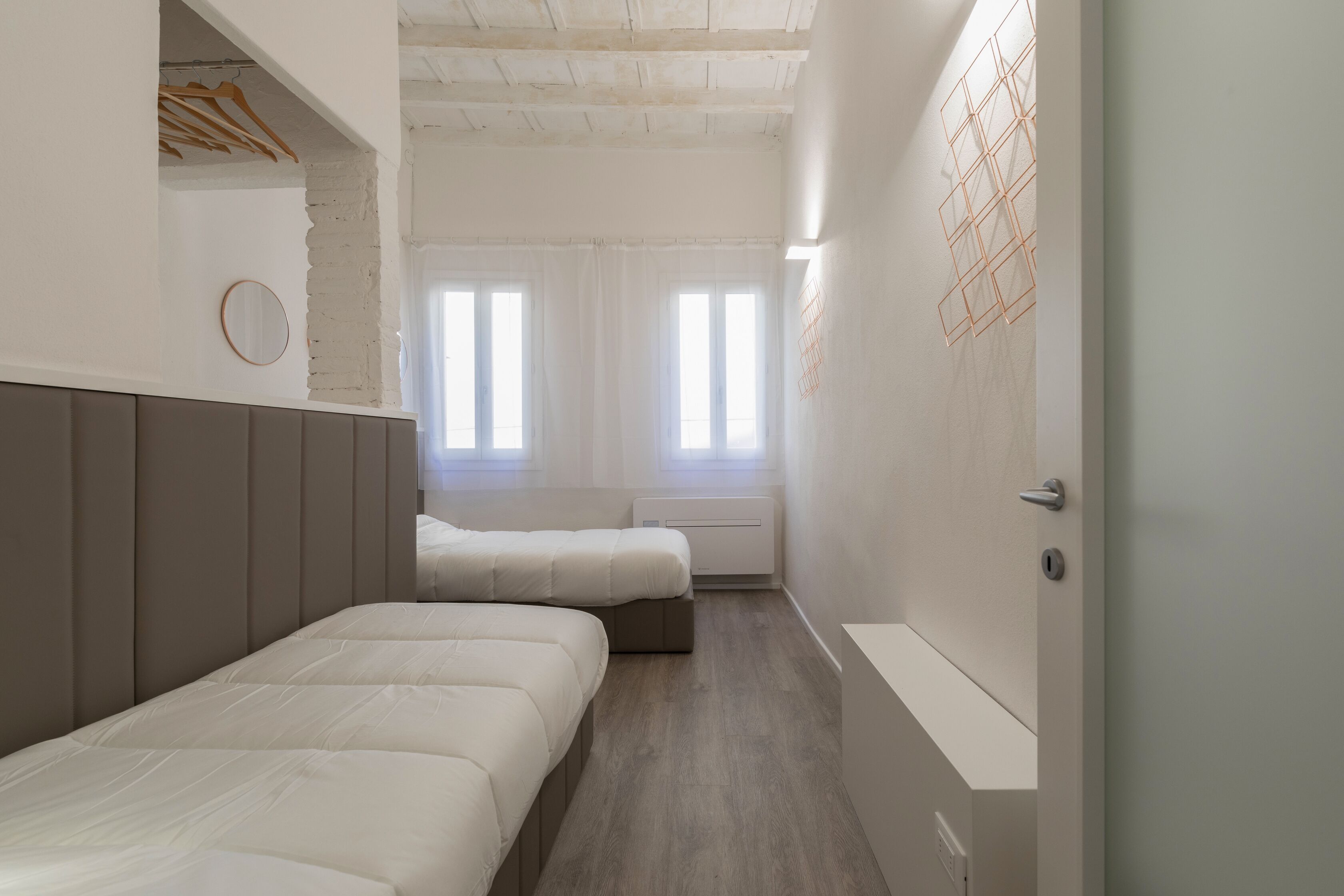 A modern hotel room with two beds, a large window, and a white wall with a geometric art piece.