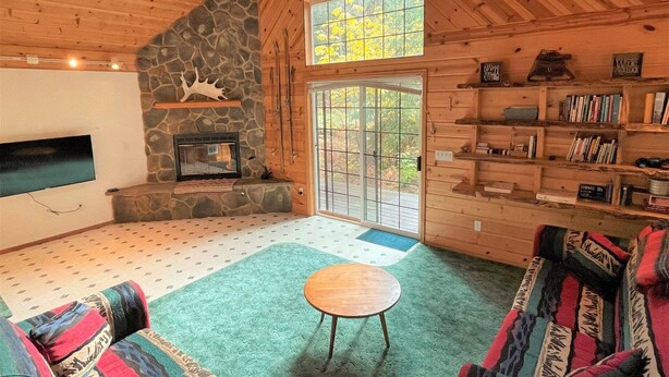 A cozy cabin interior with a stone fireplace, a large window, and a bookshelf. - Mossy Moose (Packwood)