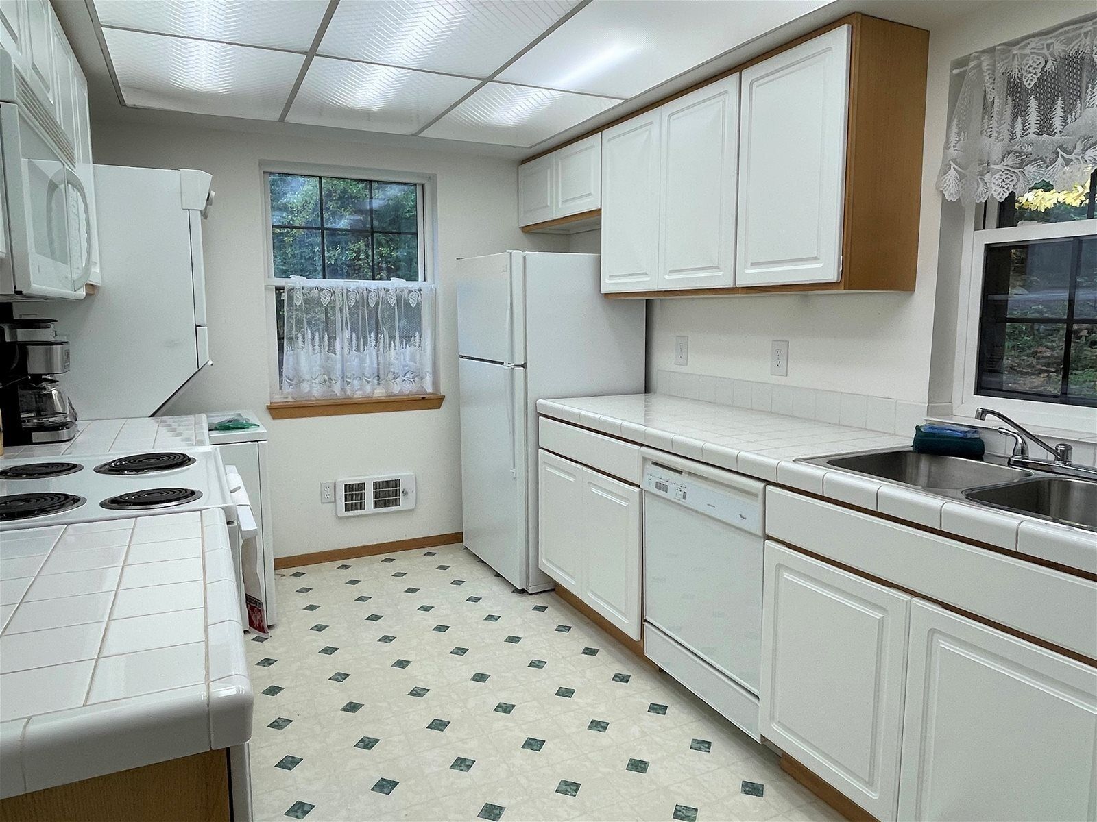 A compact kitchen with white cabinets, a stove, a refrigerator, and a dishwasher.
