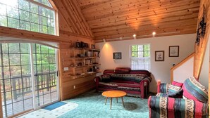 A cozy cabin interior with a large window, wooden walls, a sofa, a coffee table, and a staircase. - Mossy Moose (Packwood)