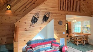 A cozy cabin interior with a wooden staircase, a colorful sofa, and a dining area with wooden furniture. - Mossy Moose (Packwood)