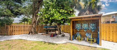 Patio trasero con terraza de madera, zona de estar cubierta y un árbol.