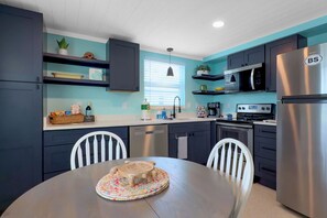 A modern kitchen with dark cabinets, a stainless steel refrigerator, and a dining table with chairs. - Turtle Cay at The Beach Shack! Come On Down! (Englewood)