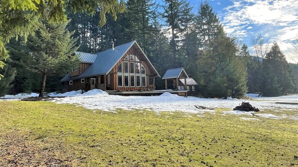 A log cabin with a large front porch and a chimney, surrounded by snow and trees. - Elkhorn (Packwood)