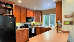 A kitchen with wooden cabinets, a black refrigerator, a microwave, a stove, and a large island with a sink. - Elkhorn (Packwood)