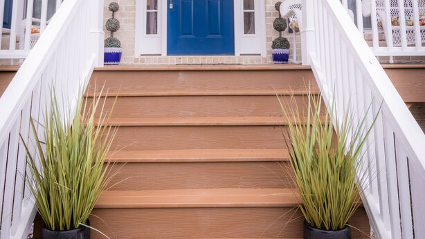 A front porch with a blue door, white railings, and potted plants.