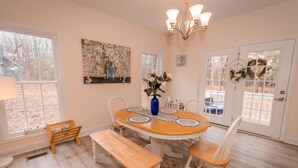 A dining area with a round table, white chairs, a bench, and a vase of flowers.