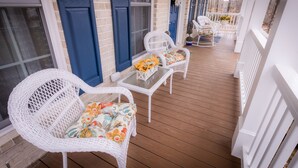 A covered porch with white wicker chairs and a glass table, blue doors, and a brick wall.