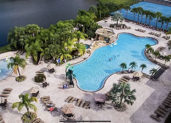 Relax by the resort's large, curved pool surrounded by lounge chairs and palm trees, with additional pools and a tennis court nearby.