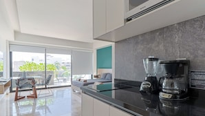 A modern kitchen with a black countertop, a coffee maker, and a blender. There is a dining area with chairs and a table in the background. - Torre Diez by Grupo Amber (Playa del Carmen)
