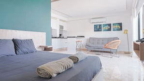A modern hotel room with a bed, a sofa, a chair, a kitchen area, and artwork on the walls. - Torre Diez by Grupo Amber (Playa del Carmen)