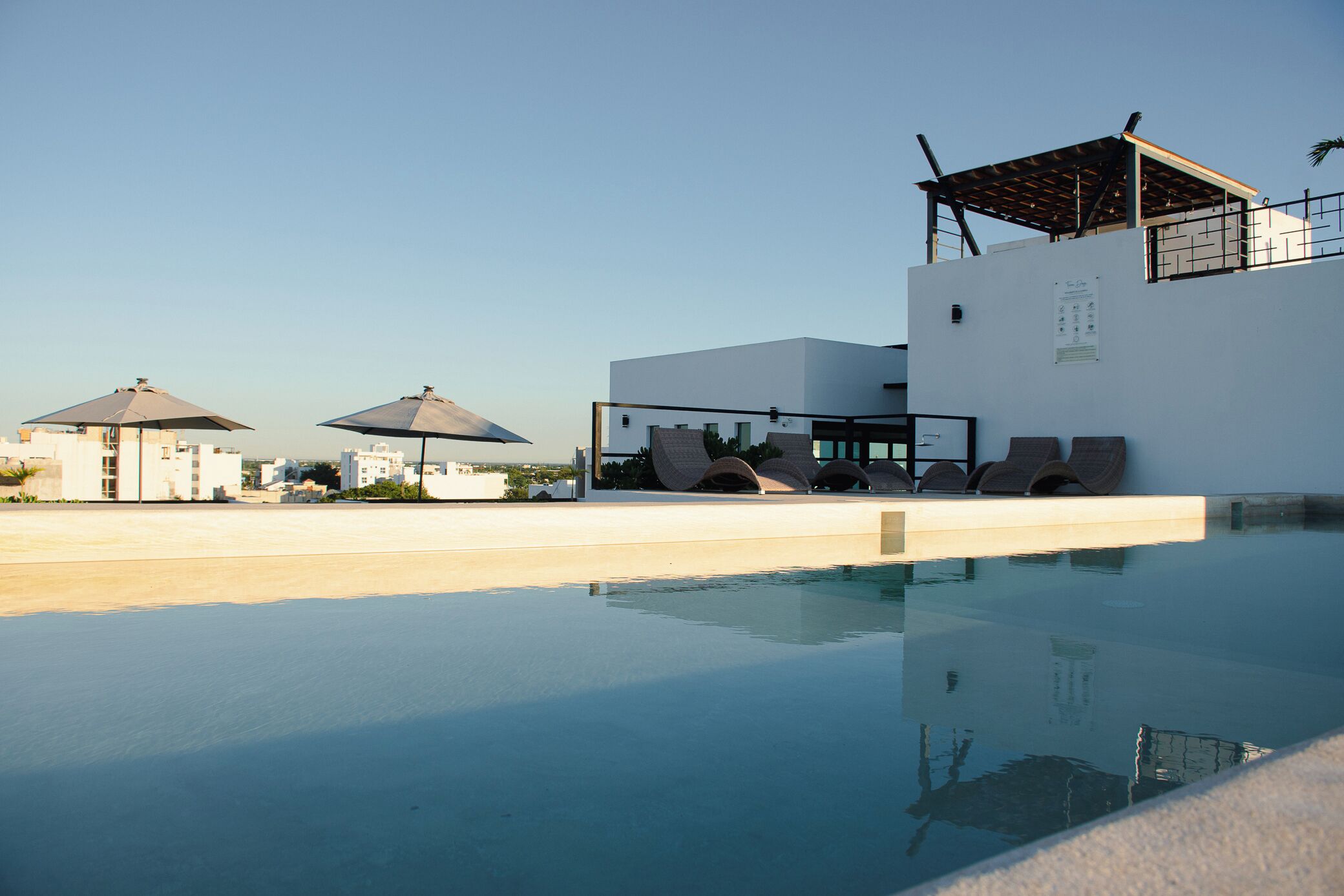 Una piscina con sillas de descanso y sombrillas, un área de estar cubierta y vistas de edificios circundantes.