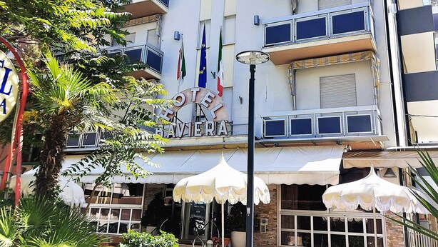A hotel with multiple balconies, outdoor seating, and flags. - Hotel Baviera (Chioggia)