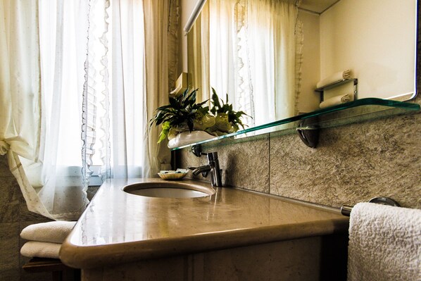 A bathroom with a marble sink, a glass shelf above the sink, and a towel rack. - Hotel Baviera (Chioggia)