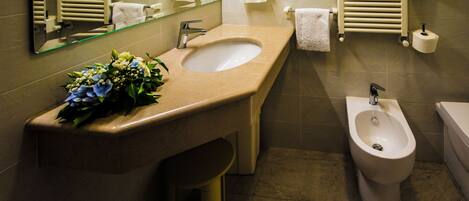 A bathroom with a sink, bidet, and a mirror. There is a towel rack and a toilet paper holder on the wall.