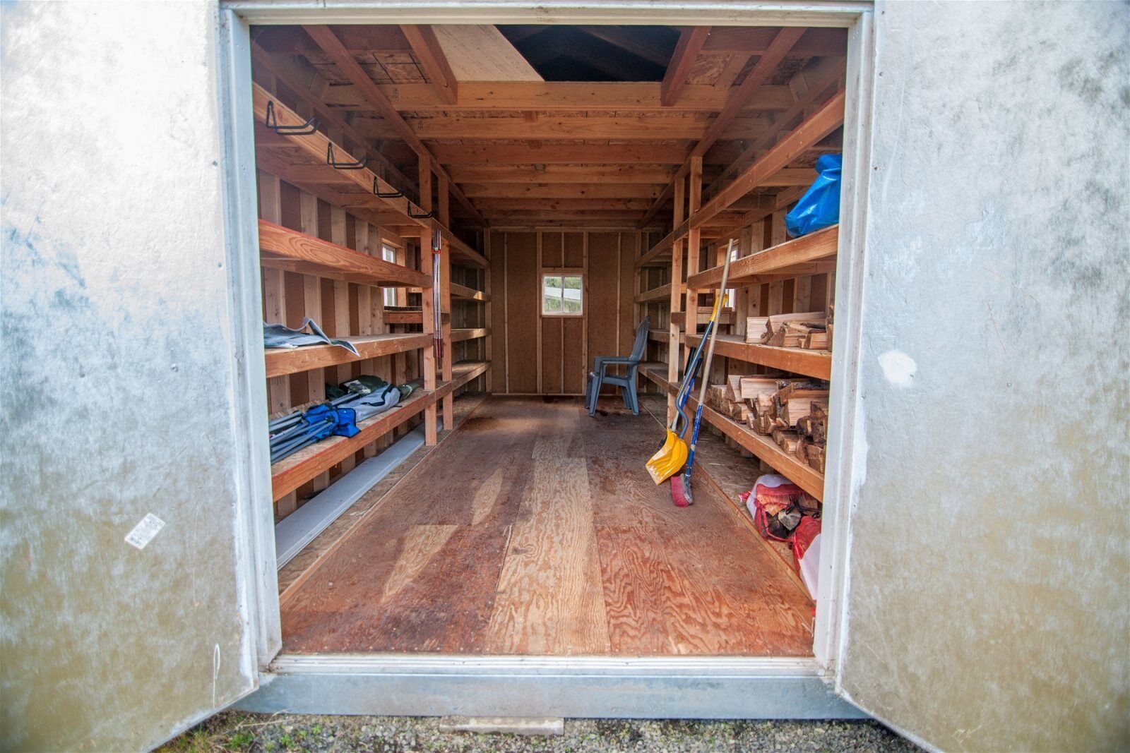 A wooden interior with shelves on both sides, a chair in the center, and a broom leaning against the right wall.