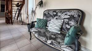 A room with a wooden ceiling, a black and white patterned sofa, a potted plant, and a ladder against the wall. - Old farmhouse 100m², quiet, 500 m from the beach, sleeps 6-9 (Saint-Michel-en-Grève)