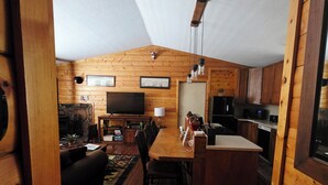 Un accogliente interno di una baita con arredamento in legno, zona pranzo, camino e cucina.