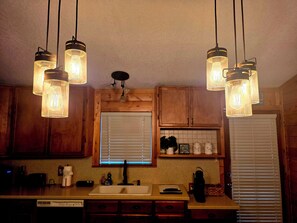 A kitchen with wooden cabinets, a window with blinds, a sink, and pendant lights.