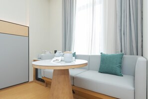 Moderni huone, jossa on pyöreä puinen pöytä, vaaleanharmaa sohva, jossa on turkoosi koristetyyny, ja ikkuna, jossa on läpikuultavat verhot.