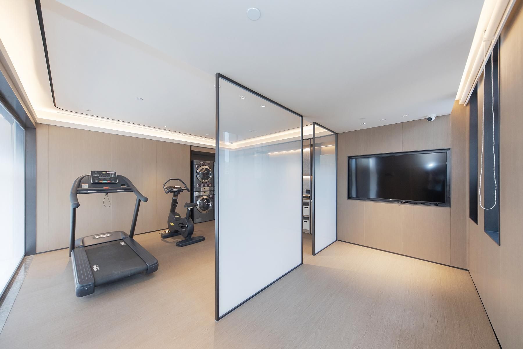 A modern room with a treadmill, stationary bike, and a flat-screen TV mounted on the wall.