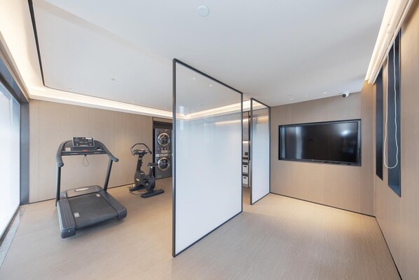 A modern room with a treadmill, stationary bike, and a flat-screen TV mounted on the wall.
