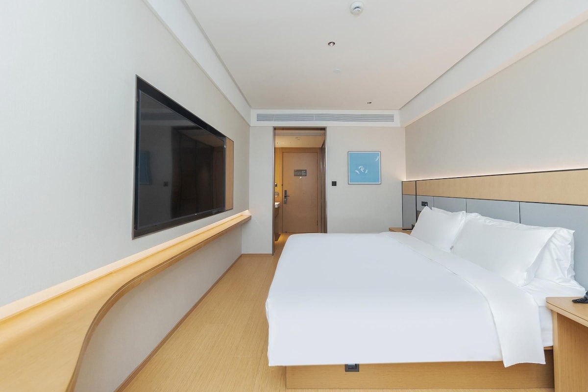 A hotel room with a bed, a television, a door, and a small table.