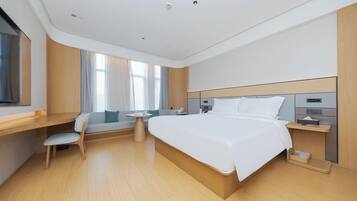A modern hotel room with a large bed, a desk, a chair, a small table, and a window with curtains.