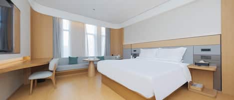 Quarto de hotel moderno com uma cama grande, uma escrivaninha, uma cadeira, uma mesinha e uma janela com cortinas.