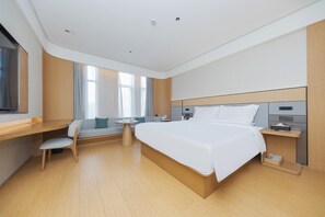 A modern hotel room with a large bed, a desk, a chair, a small table, and a window with curtains.