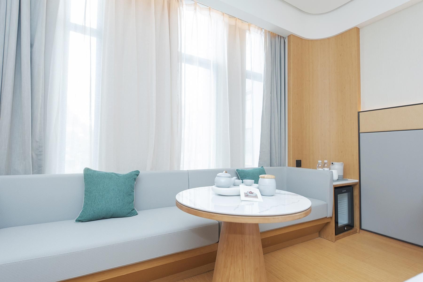 A modern room with a sofa, a round table, and a small kitchenette area.