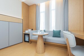 A compact room with a sofa, a small round table, and a refrigerator. - Ji Hotel (Hangzhou)