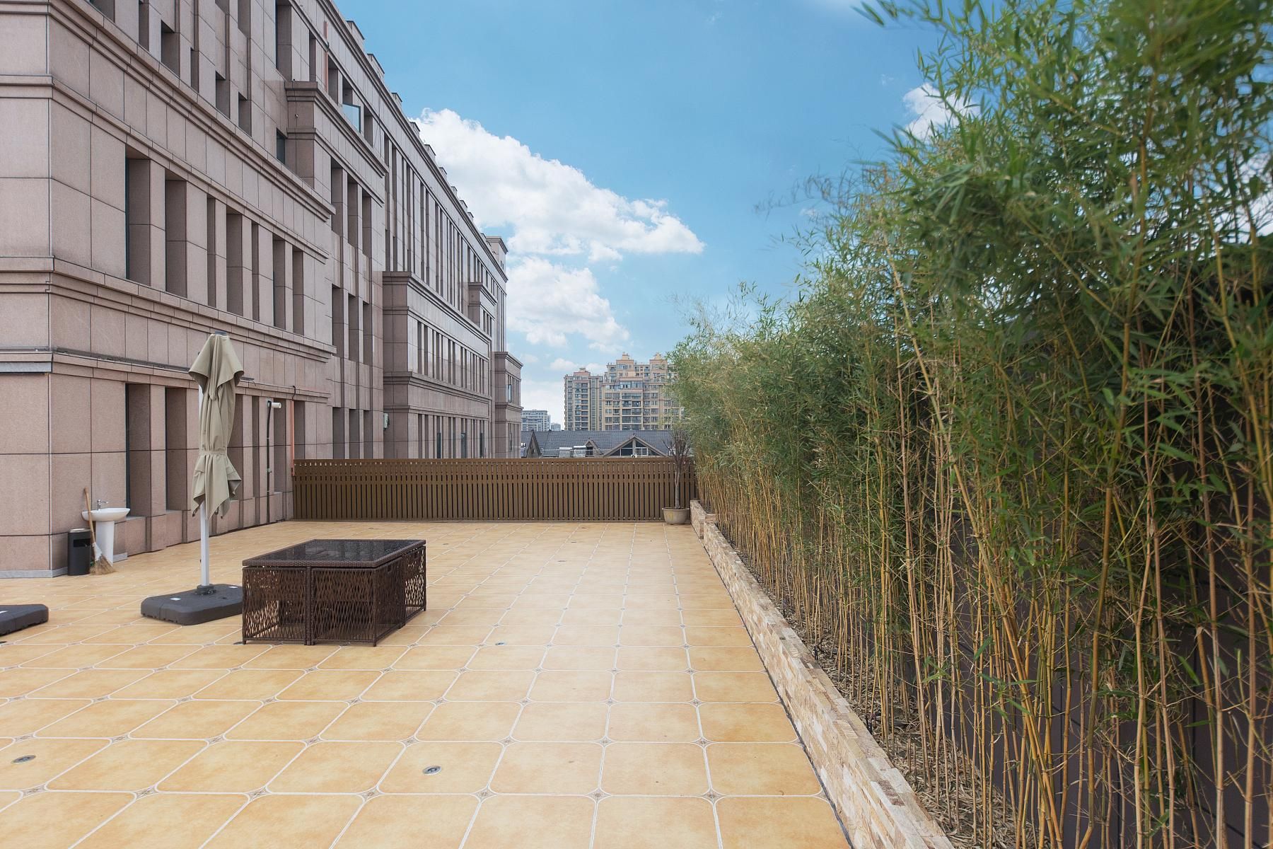 A rooftop terrace with a tiled floor, a wooden fence, and a row of bamboo plants.