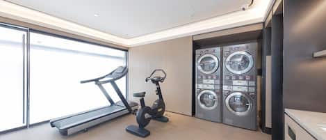 A modern gym with a treadmill, stationary bike, and a wall-mounted laundry machine.
