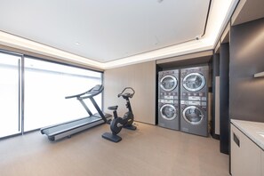A modern gym with a treadmill, stationary bike, and a wall-mounted laundry machine. - Ji Hotel (Hangzhou)