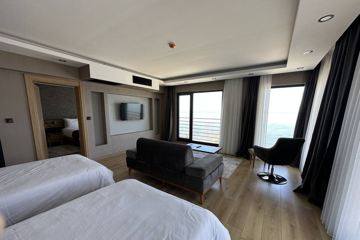 A hotel room with two beds, a sofa, a TV, a desk, and a view of the sea.