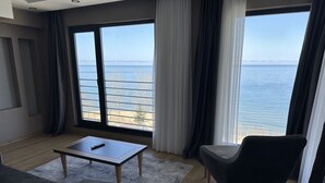A modern living room with a large window overlooking a beach and the sea. - Şehrar Suit Hotel (Surmene)
