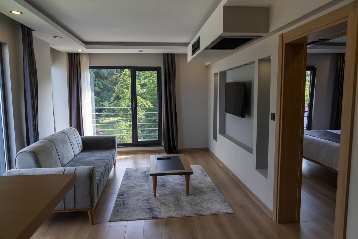 A modern living room with a grey sofa, a wooden coffee table, and a large window with curtains.