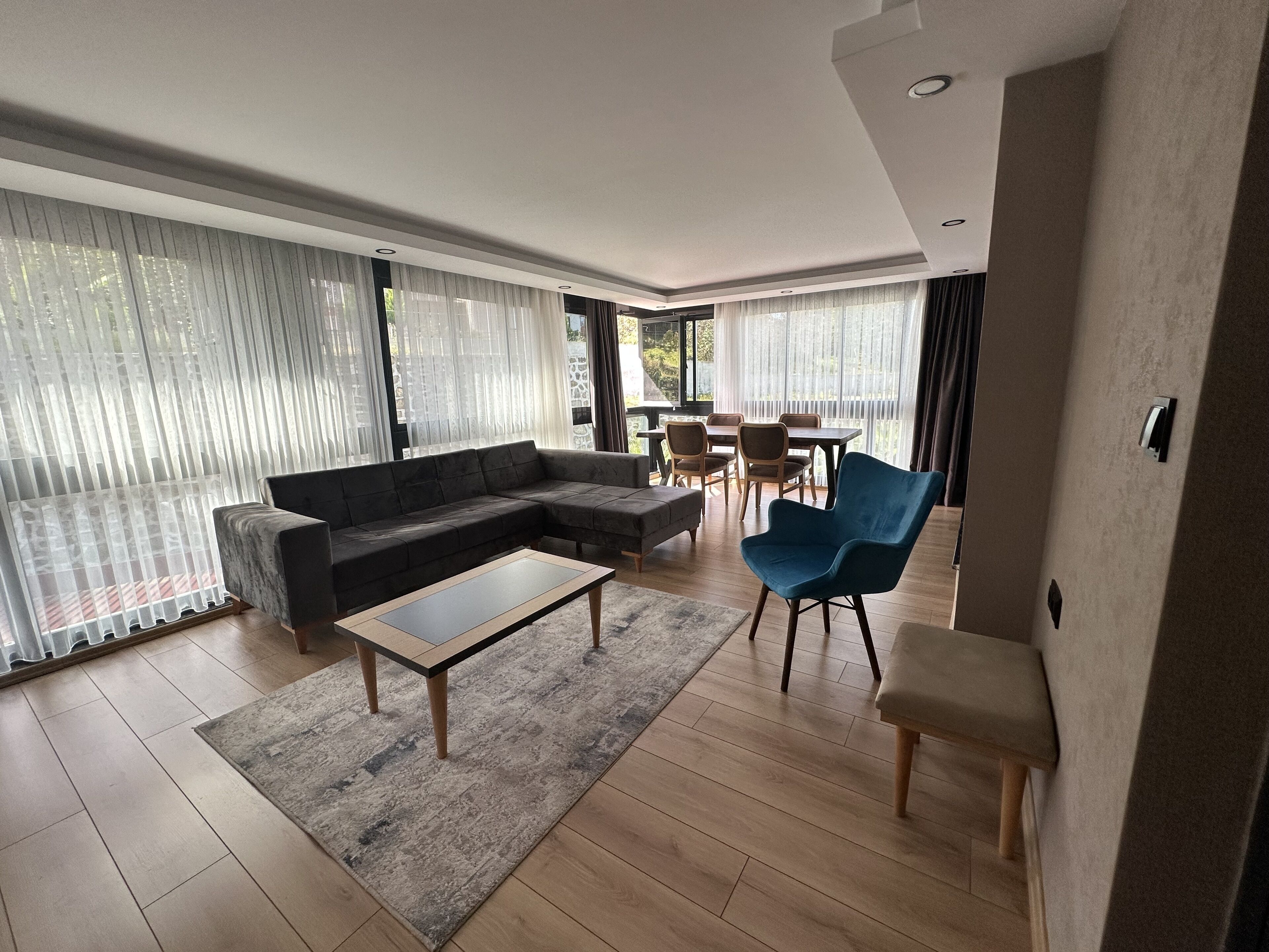 Un salon moderne comprenant un canapé d’angle, un fauteuil bleu, une table basse et un coin repas avec une table et des chaises.