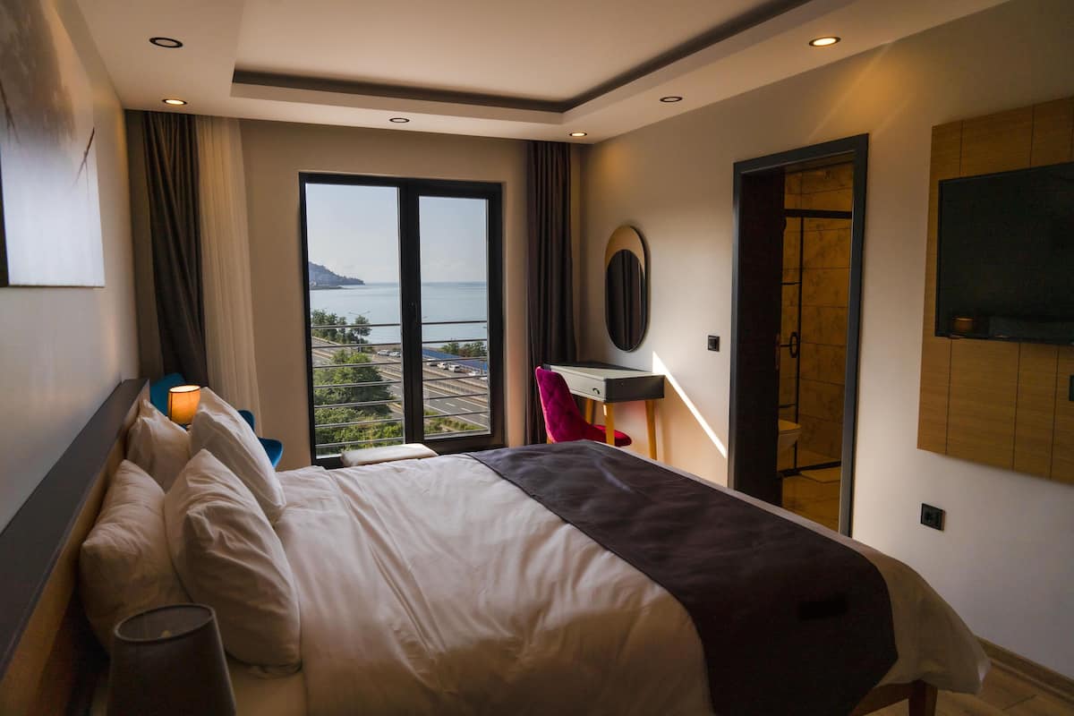 A hotel room with a large bed, a desk, a chair, a TV, and a view of the sea.